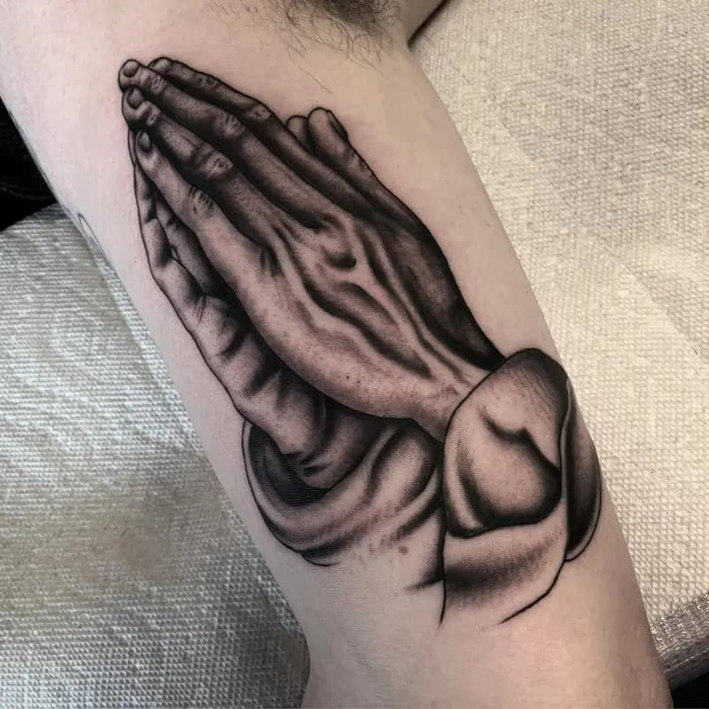 a tattoo of a hand clasped in prayer